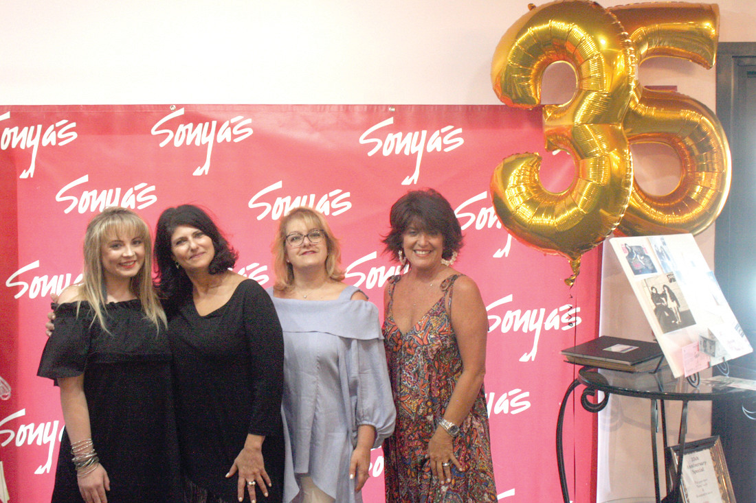 CELEBRATION: Four of the staff at Sonya’s Clothing, including (from left) Kylie Pimental, a college student who started working there in high school, Sonya Gasparian-Janigian, Rena Megrdichian, the office manager, and Lori Pesce, a retail associate, pose in front of their celebration wall, which would be used for photos all weekend during the open house.